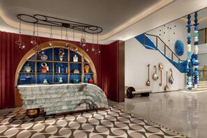 A modern interior with a marble table, a blue and gold arched shelf, and a staircase with blue and white decor. - Renaissance Korla Hotel (Korla)