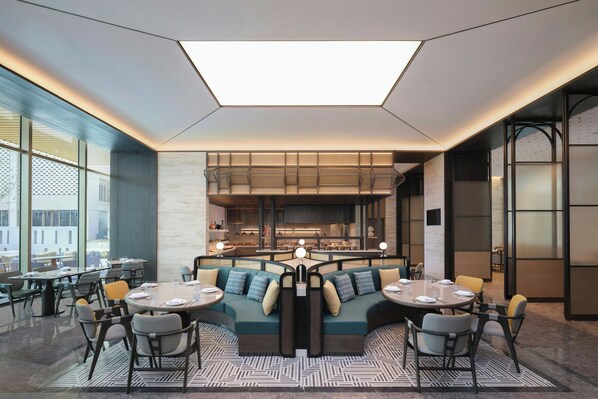 A modern restaurant with a central seating area, large windows, and a geometric ceiling design. - Courtyard By Marriott Korla (Korla)