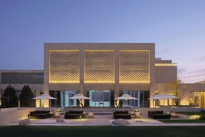 Un edificio moderno con fachada geométrica, amplios ventanales y zona de estar exterior con sombrillas.