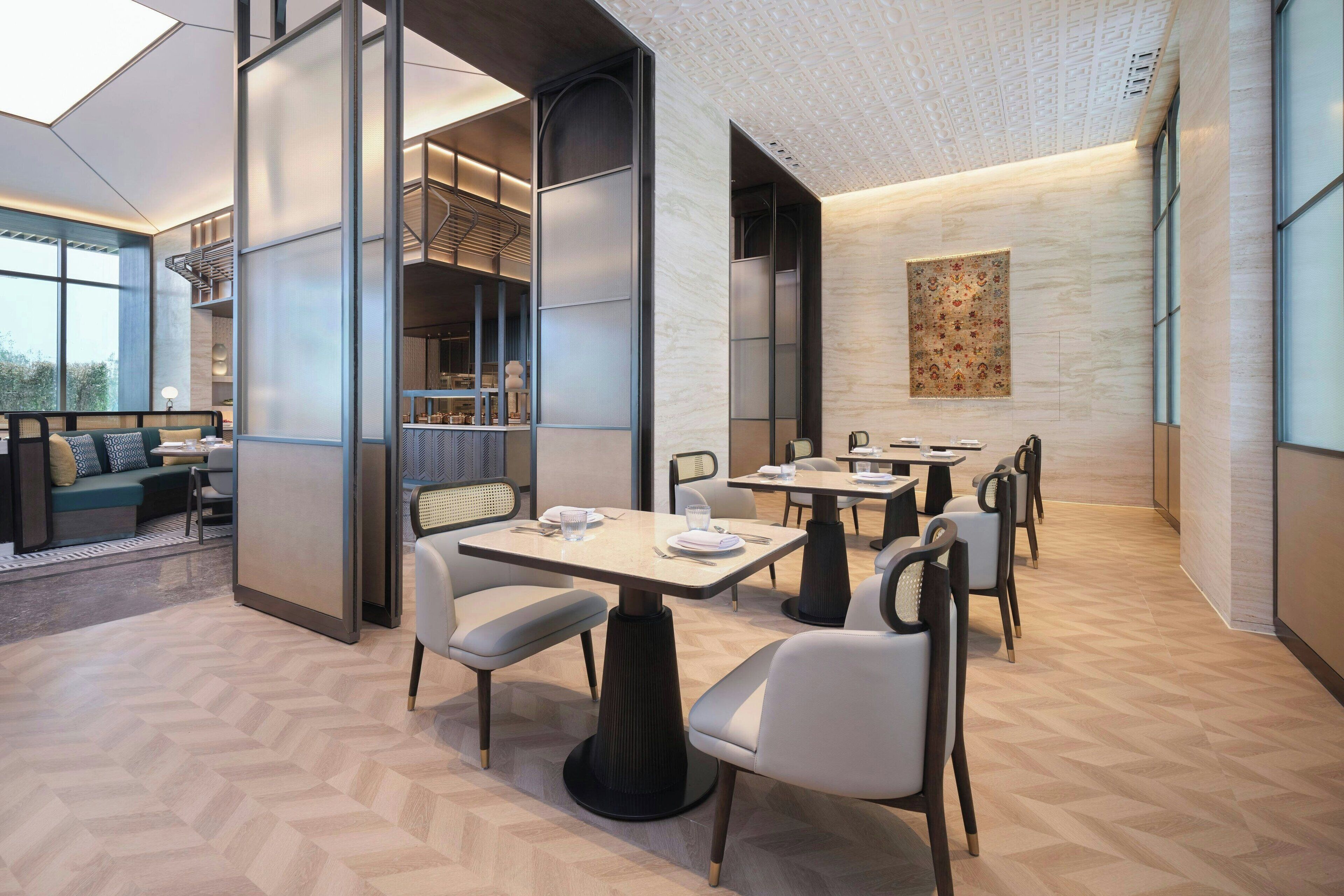 A modern dining area with tables and chairs, a sofa, and a large window.