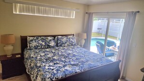 Un dormitorio con cama, dos lámparas de noche, una ventana con persianas y vista a una piscina.