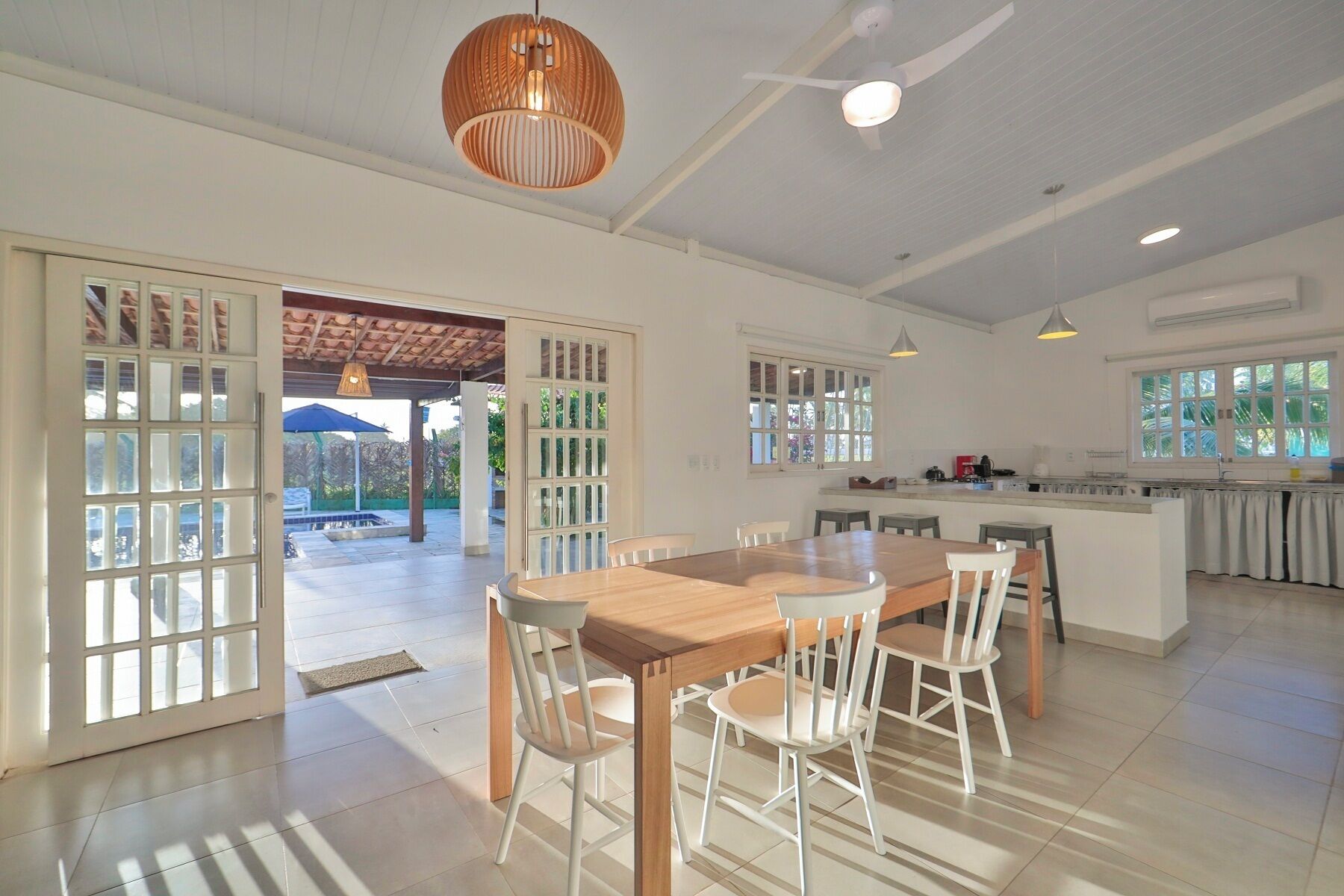Una cocina amplia con una isla central, ventanas grandes y un comedor con mesa de madera y sillas blancas.