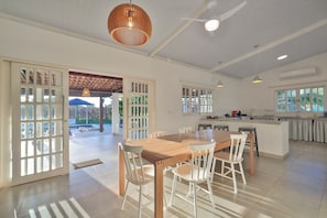 A spacious kitchen with a central island, large windows, and a dining area with a wooden table and white chairs. - Pousada Xalés de Maracaípe (Ipojuca)