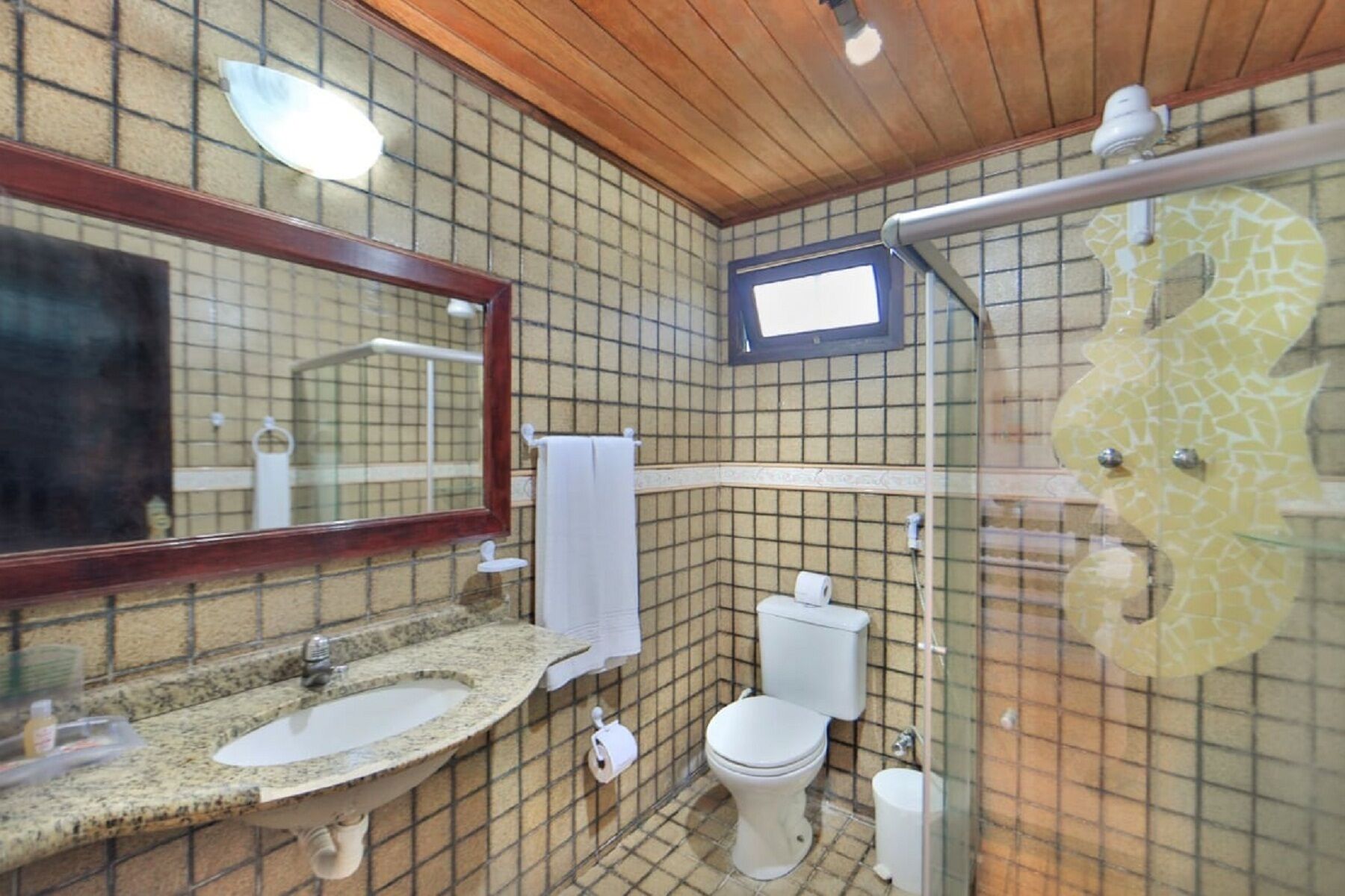 Une salle de bain avec un carrelage au sol, un lavabo avec un miroir, des toilettes et un espace douche.
