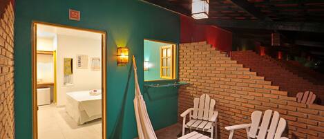 A room with a brick wall, a hammock, and two Adirondack chairs.