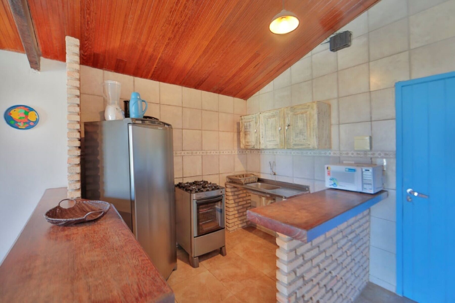 Una cucina compatta con soffitto in legno, piano cottura integrato, frigorifero e forno a microonde.