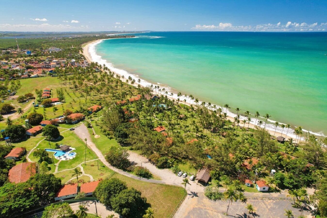 An aerial view of a coastal resort with a beachfront, palm trees, and a swimming pool.