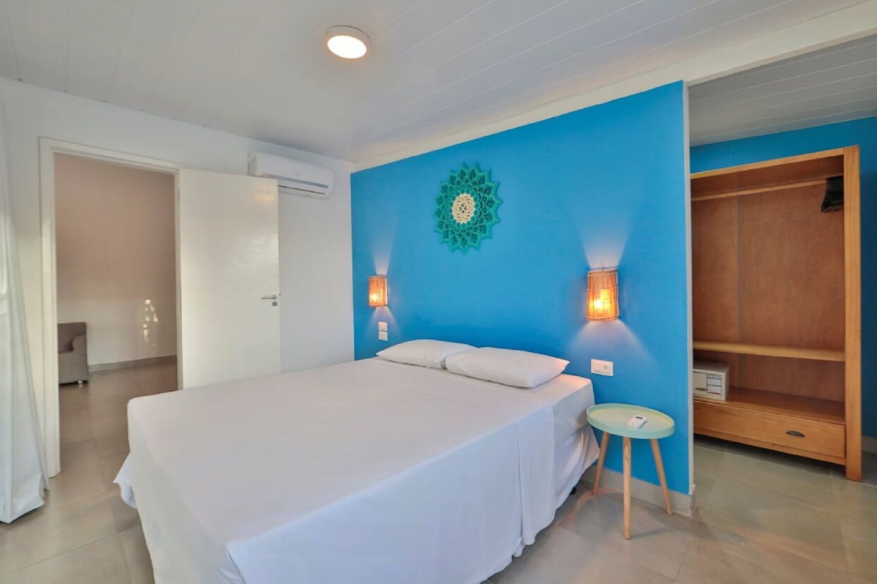 Un dormitorio con una cama grande, dos lámparas de pared, una pared azul decorativa y un armario de madera.