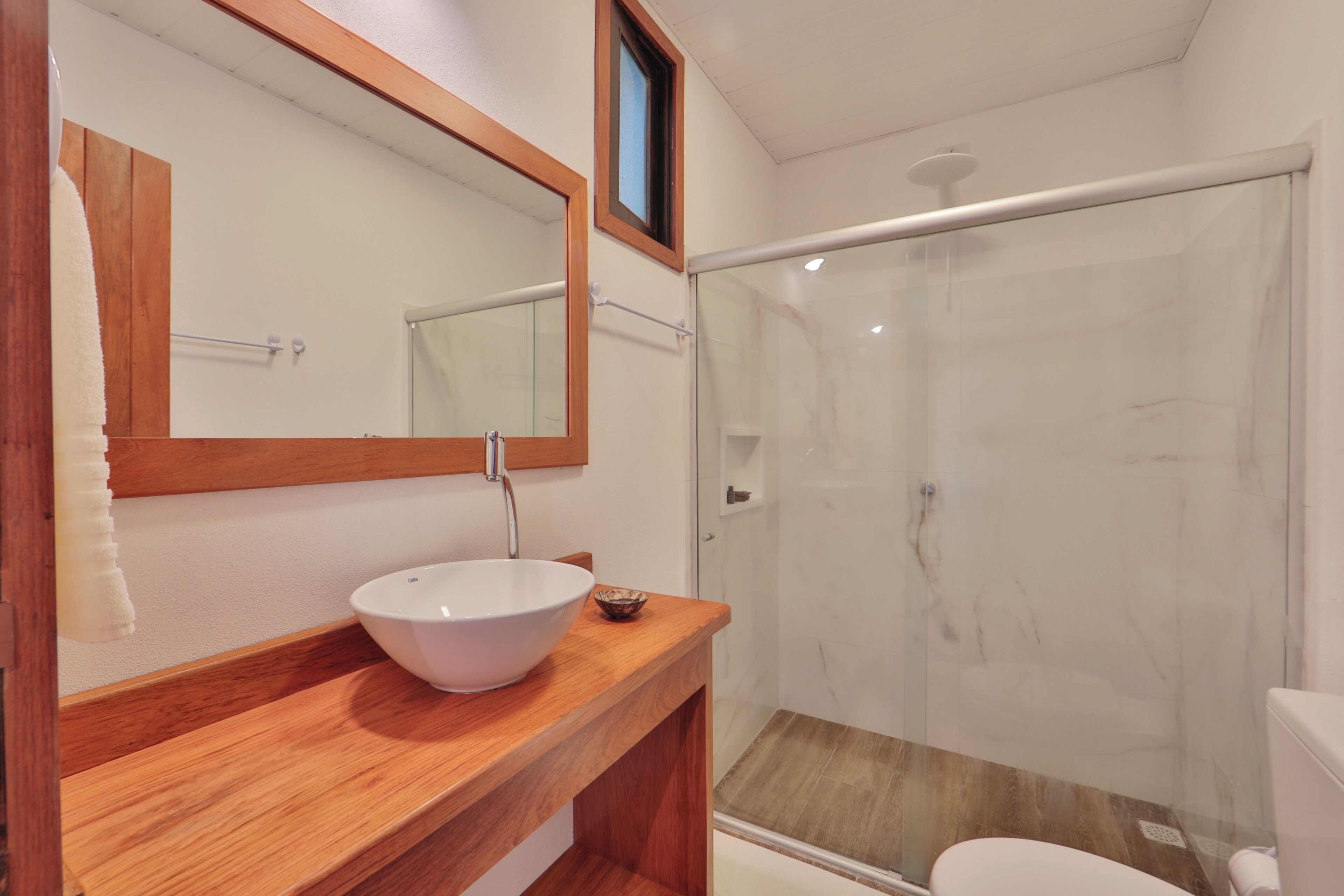 A bathroom with a wooden vanity, a white sink, a mirror, and a glass shower enclosure.