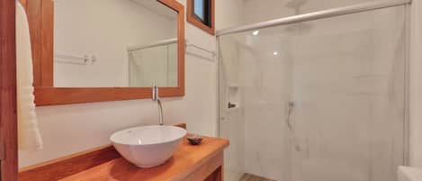 A bathroom with a wooden vanity, a white sink, a mirror, and a glass shower enclosure.