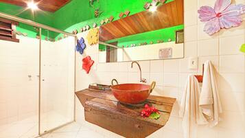 Een badkamer met een douchecabine van glas, een houten wastafelmeubel met een grote waskom en een spiegel boven de wastafel.