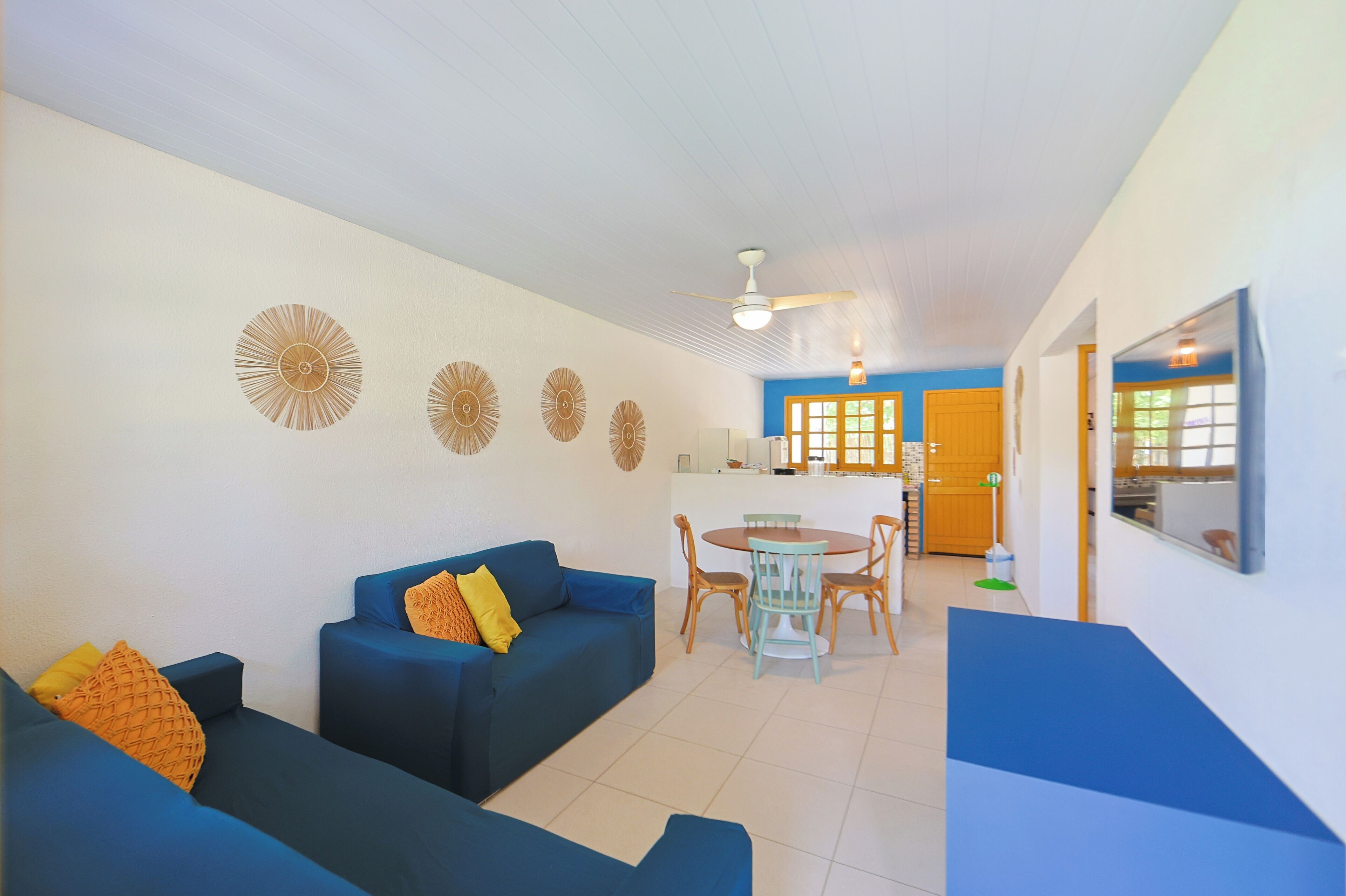 A living room with a blue sofa set, a dining table with chairs, and a ceiling fan.
