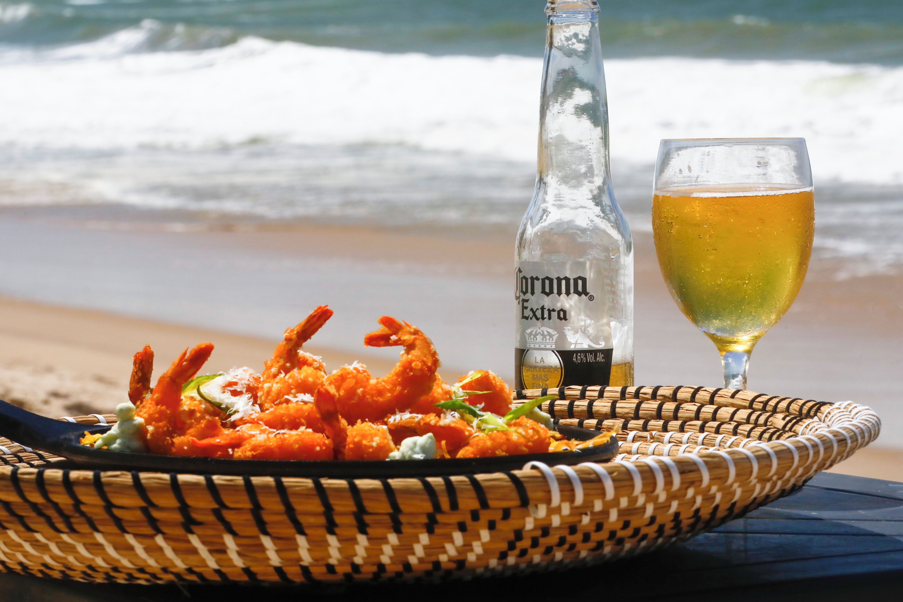 Mesa frente al mar con una cesta de camarones fritos, una botella de Corona Extra y un vaso de cerveza.