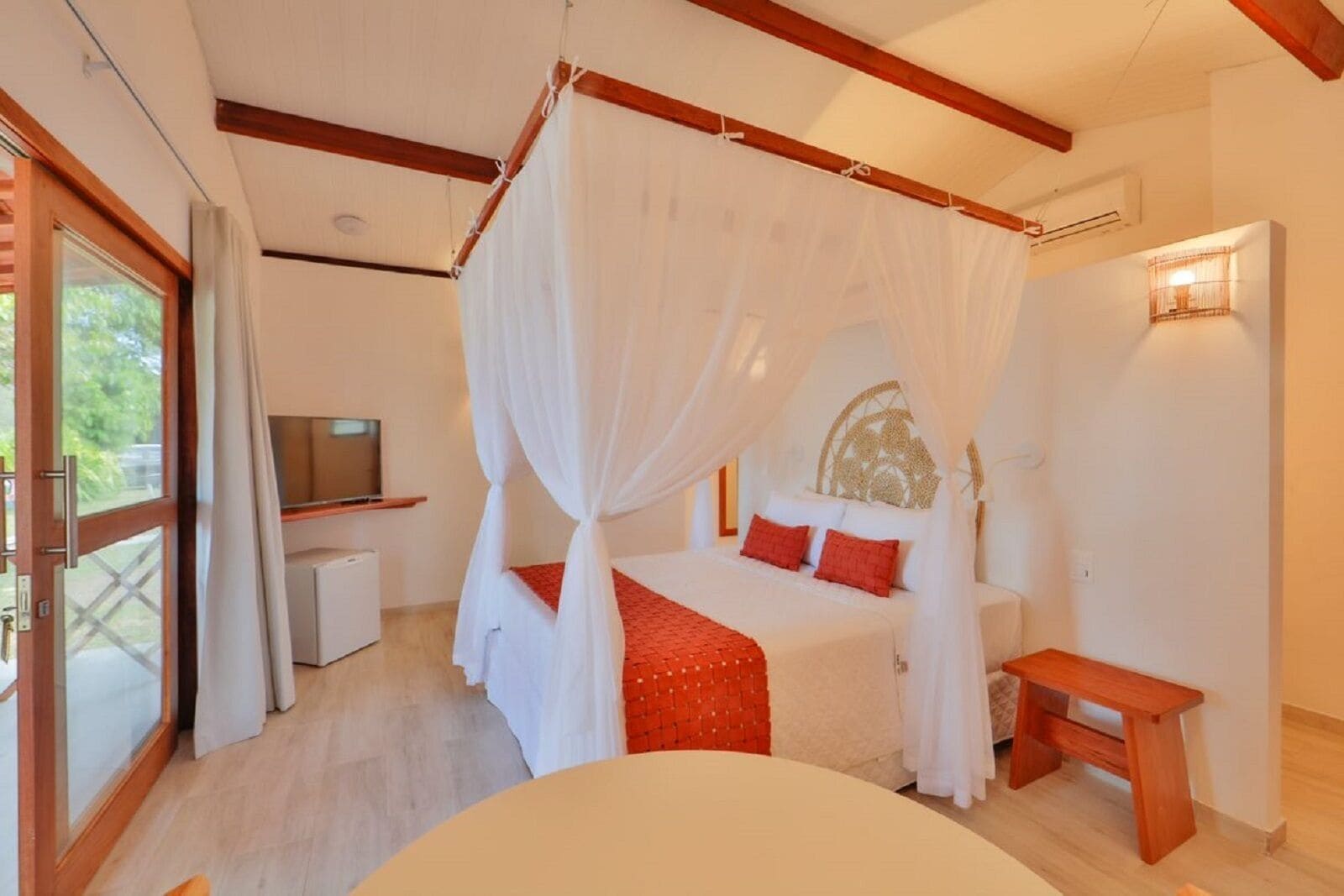 A bedroom with a canopy bed, a television, and a wooden bench.