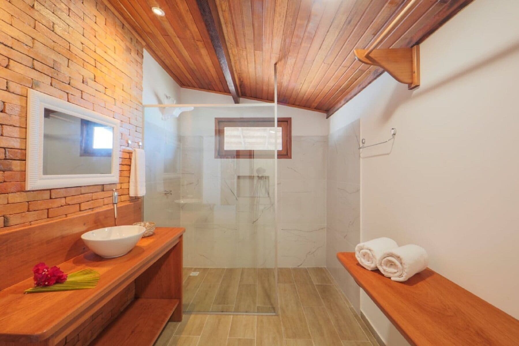A modern bathroom with a wooden vanity, a large mirror, a glass shower enclosure, and a towel rack.