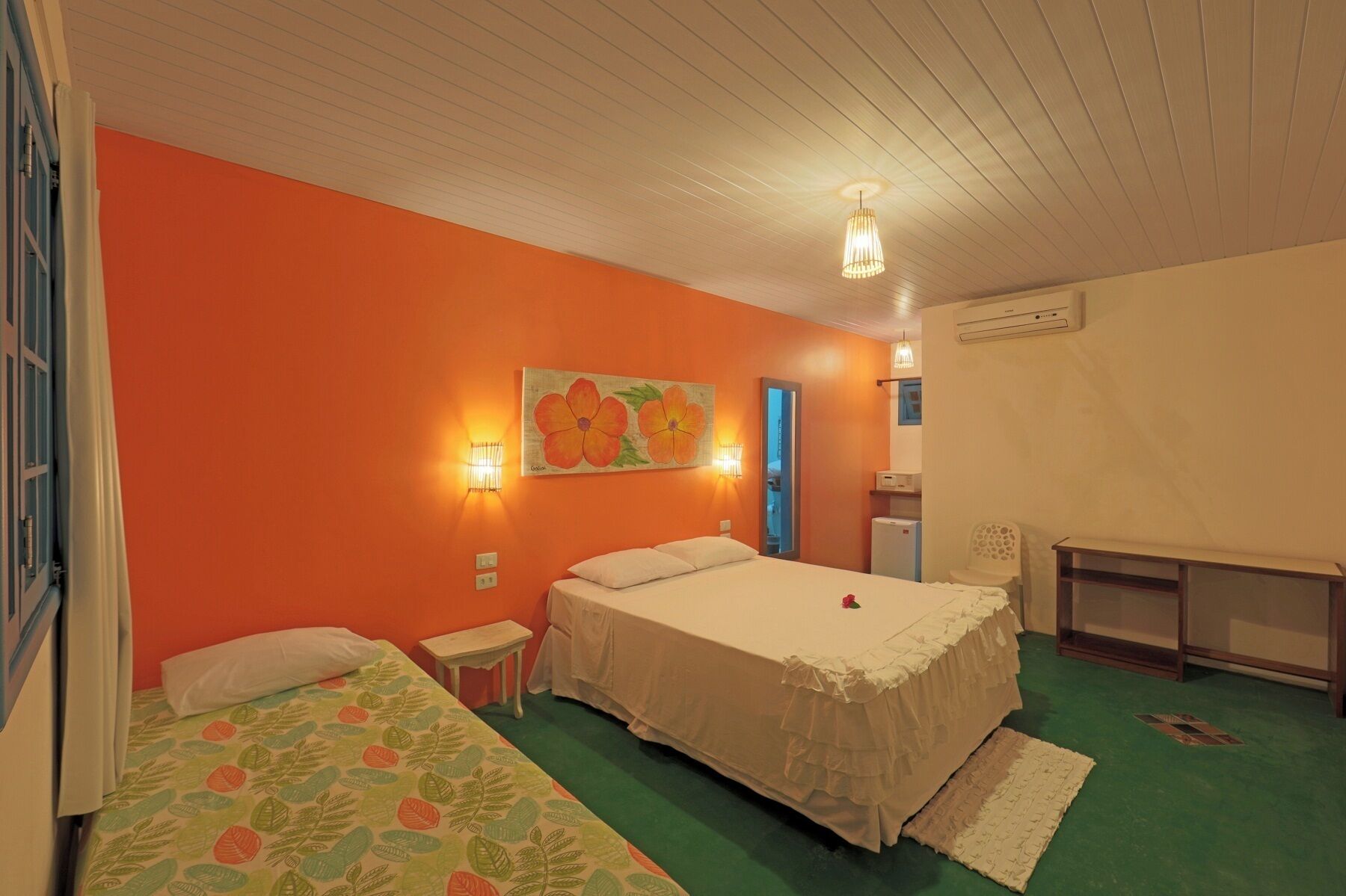 Quarto com duas camas, um quadro de flores na parede, ar condicionado fixado na parede e uma pequena mesa.