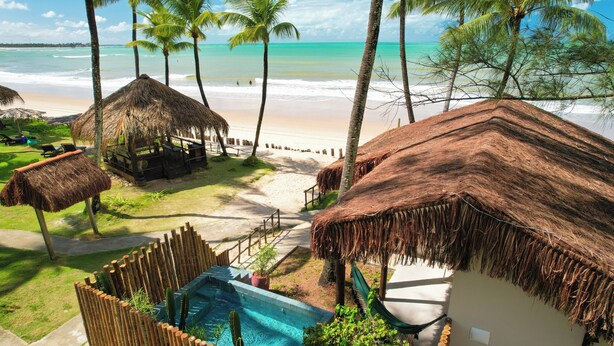 A beachside resort with thatched-roof huts, a swimming pool, and a view of the ocean. - Pousada Xalés de Maracaípe (Ipojuca)