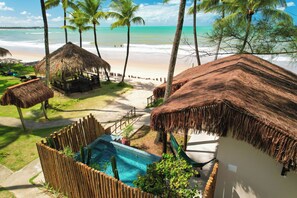 Un resort con cabañas de techo de paja, piscina y vista a la playa.