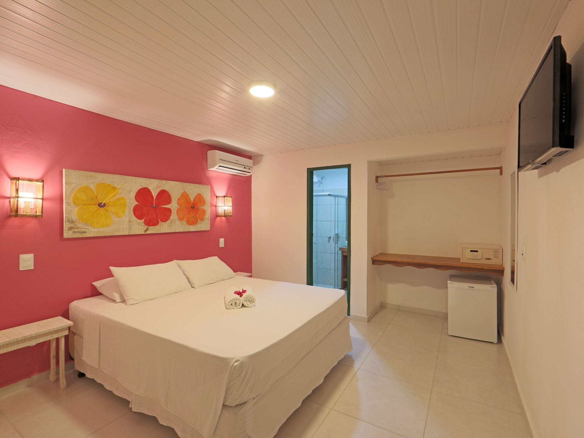 A bedroom with a bed, a desk, a chair, a TV, and a shower area.