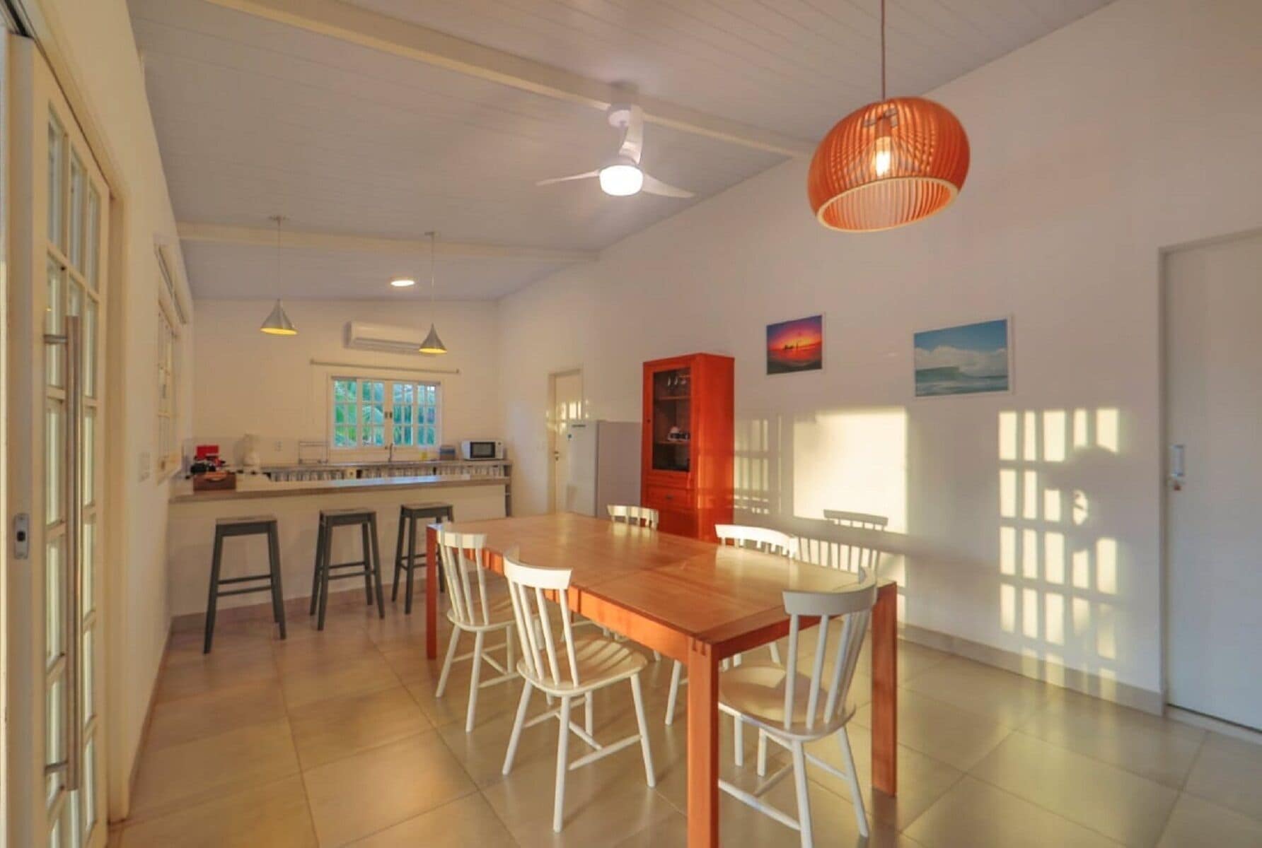 A spacious dining area with a wooden table and white chairs, a kitchen with a window, and a ceiling fan.