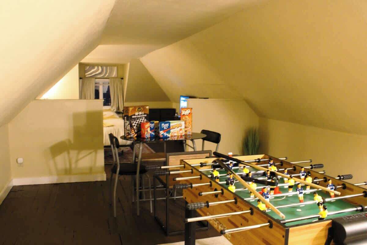 A room with a foosball table, a dining table with chairs, and a window with curtains.