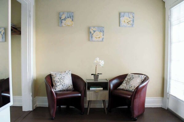 A room with two leather armchairs, a small table with a plant, and three floral paintings on the wall. - Rooftop Patio & Games in Historic Highlands (Louisville)