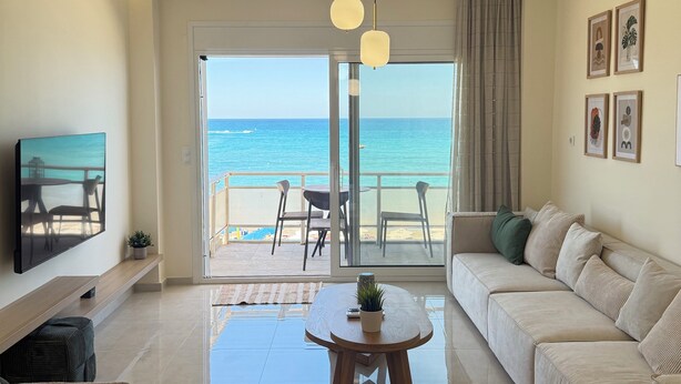 A modern living room with a sofa, a coffee table, and a TV on a wall. There is a balcony with a view of the sea. - Seaview Paradise (Rethymno)