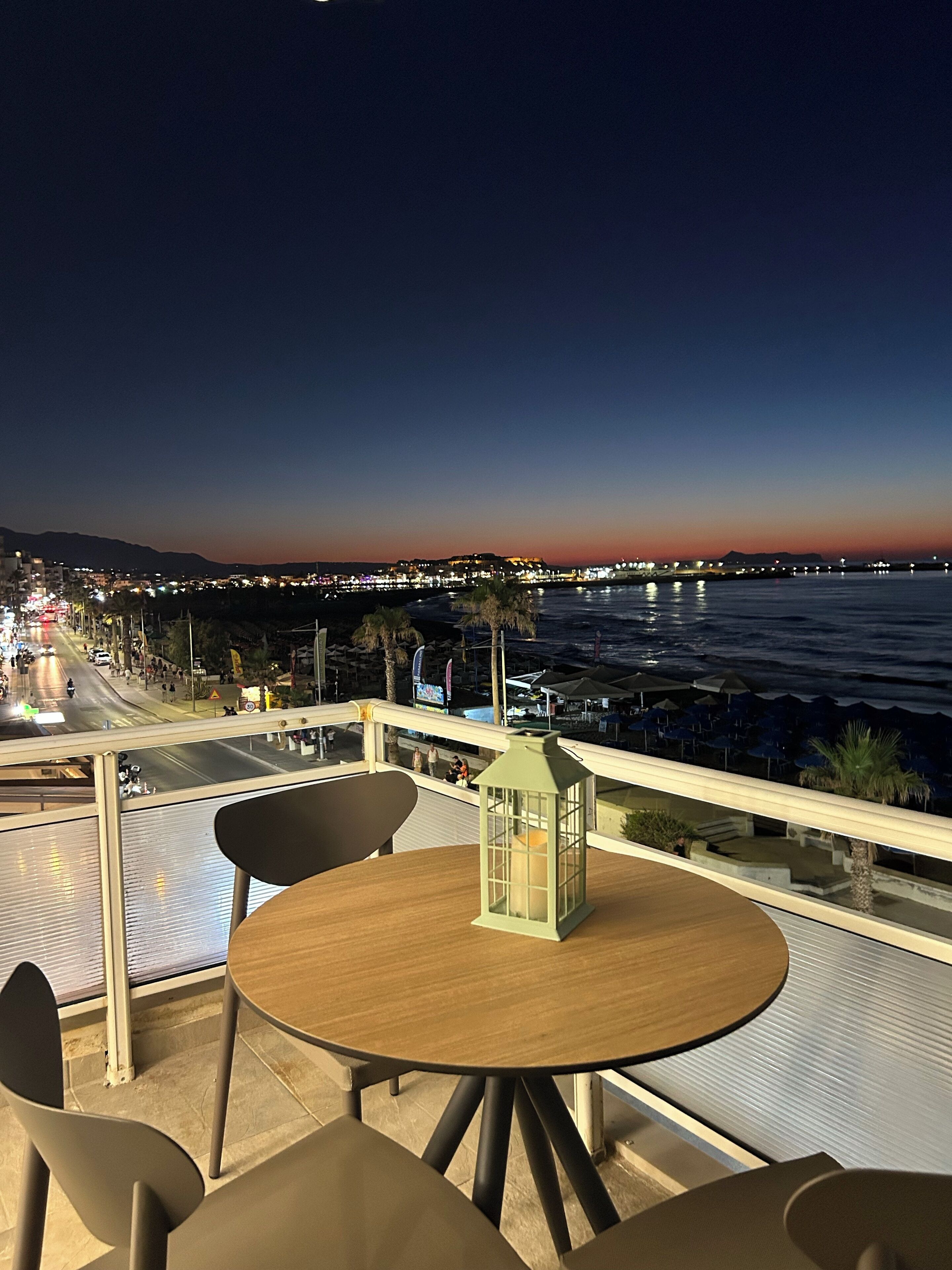 A terrace with a table and chairs, overlooking a coastal cityscape with a view of the sea and a bridge.