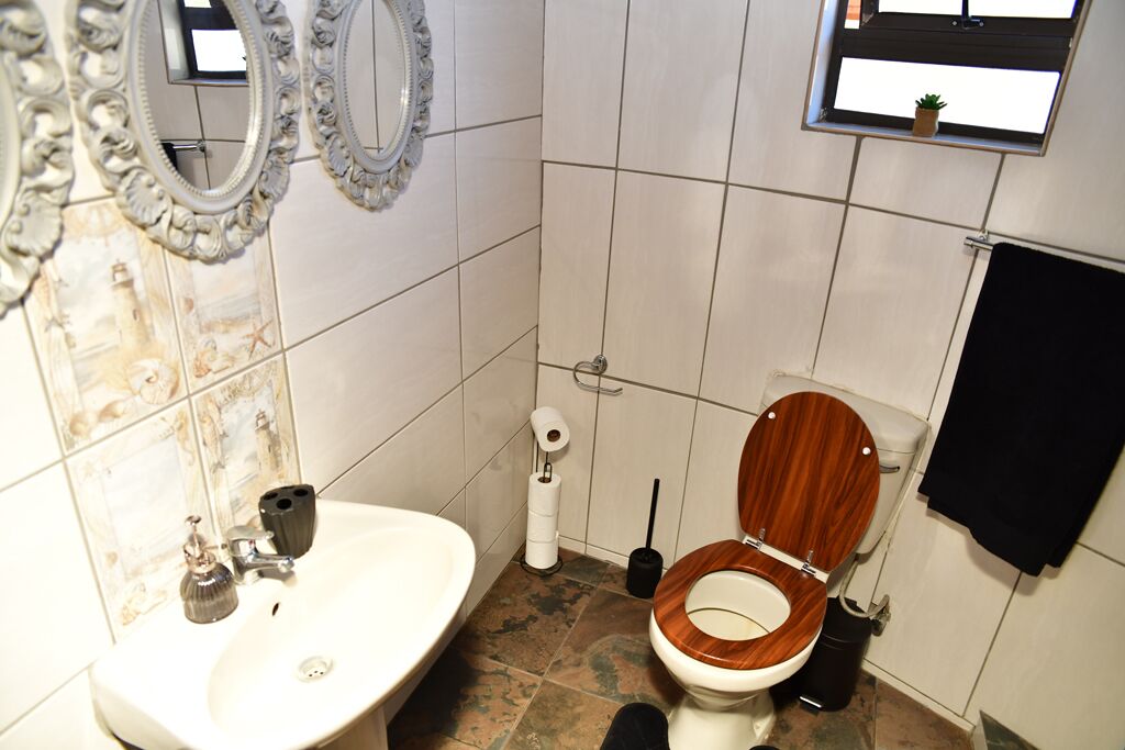 Et badeværelse med toilet i træ, hvid vask og to dekorative spejle.