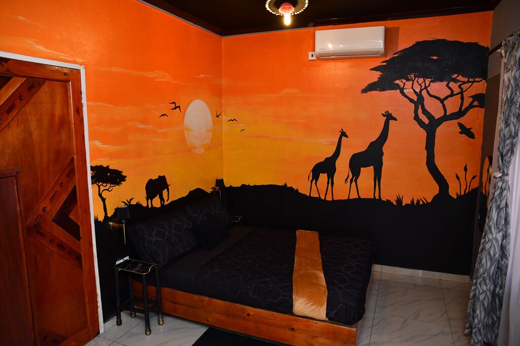 A room with a bed, a small table, and a mural of a savannah scene.