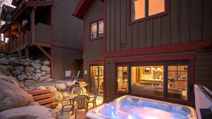 A wooden house with a hot tub, outdoor seating, and a stone wall.