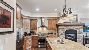 A modern kitchen with wooden cabinets, stainless steel appliances, a stone fireplace, and a granite countertop.