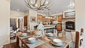 A spacious kitchen with wooden cabinets, a stone fireplace, and a dining area set for six with a large wooden table.
