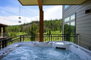 A hot tub on a balcony with a view of a forested mountain range.