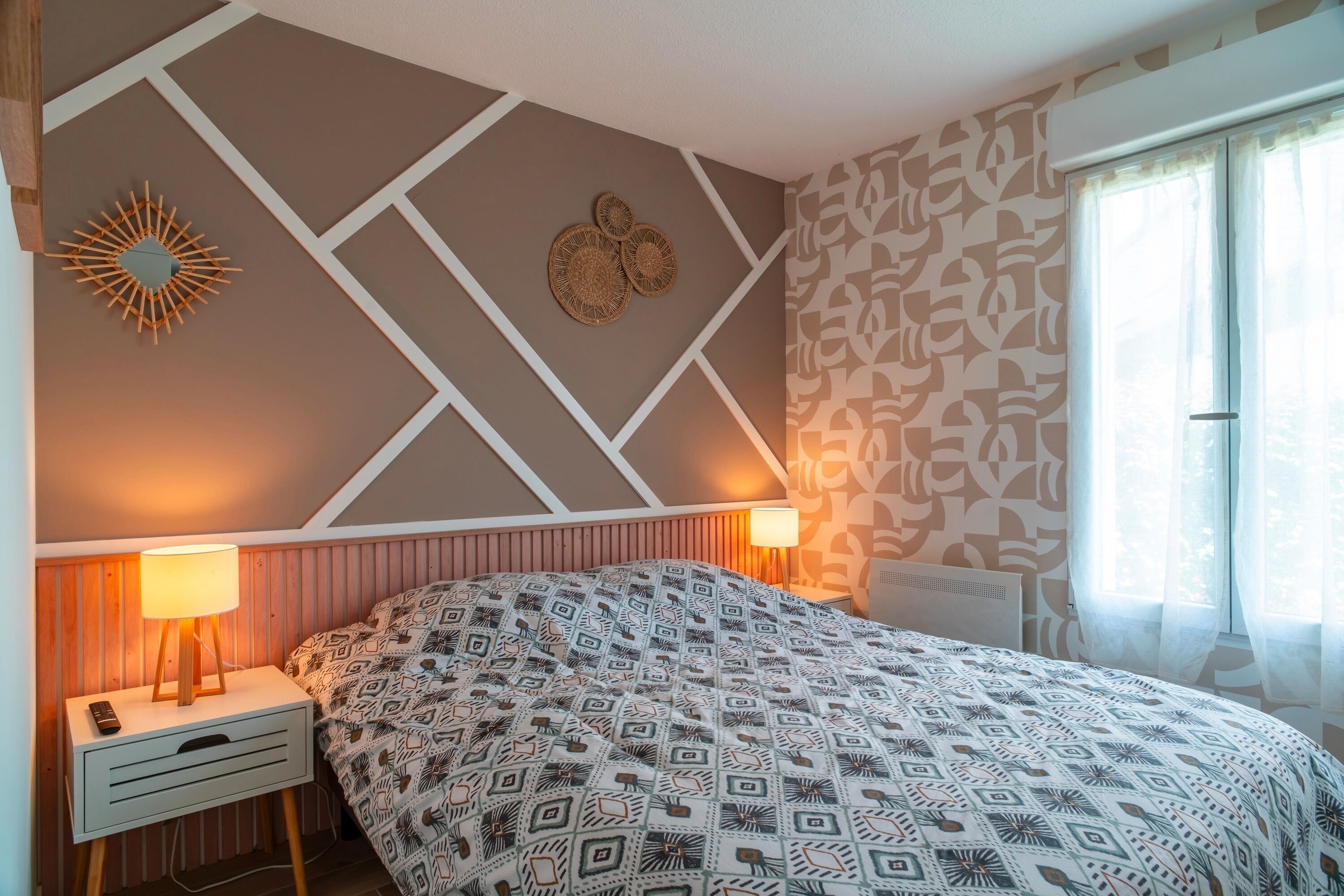Een slaapkamer met een bed met een patroon, een decoratief object aan de muur en een bedlampje.