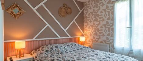 Een slaapkamer met een bed met een patroon, een decoratief object aan de muur en een bedlampje.