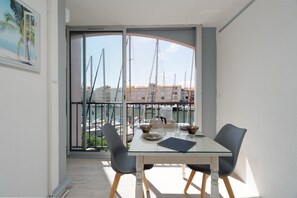 Un comedor con una mesa y sillas de vidrio, vista a un puerto deportivo con barcos, y un cuadro en la pared.