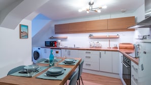 A modern kitchen with wooden cabinets, a dining table set for four, and a built-in washing machine.