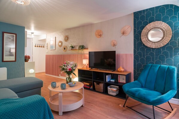 Una sala moderna con un sofá, un sillón azul, un televisor y una estantería.