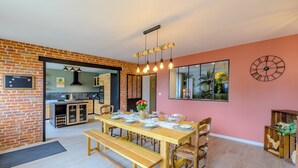 Een eetgedeelte met een houten tafel voor vier personen, bankjes en een keuken die zichtbaar is door een open doorgang.