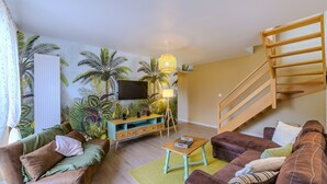 Een woonkamer met een bank, salontafel en een televisie aan een muur met een tropische muurschildering.