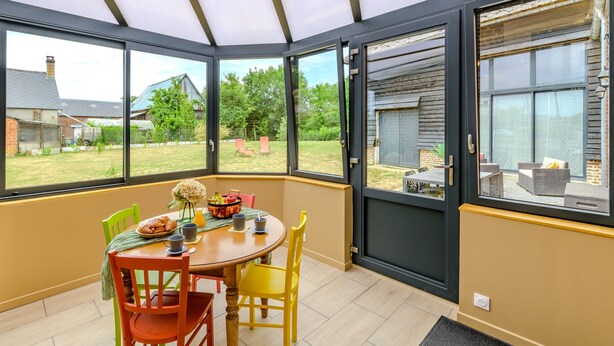 Een oranjerie met een eettafel, stoelen en een bloemstuk.