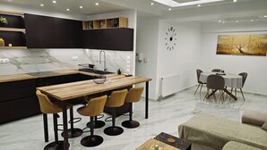 Une cuisine moderne avec un revêtement mural en marbre, un îlot central en bois doté de tabourets, et un coin repas avec une table ronde et des chaises.