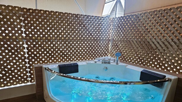 Un bain à remous avec un treillis en bois en arrière-plan et un tapis de bain noir.