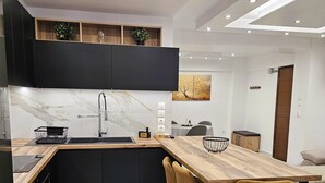 Une cuisine moderne dotée d’un plan de travail en marbre, de meubles noirs et d’une table à manger en bois, accompagnée de tabourets de bar.