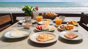 Une table de petit-déjeuner avec divers plats et boissons, le tout installé face à la plage.