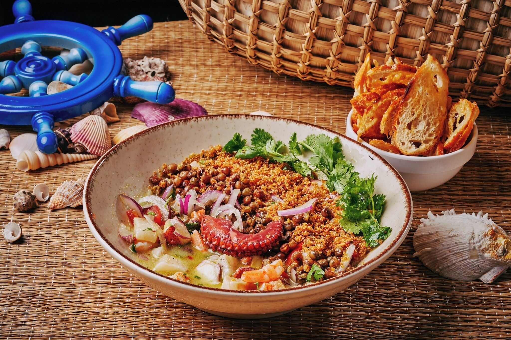 A bowl of seafood salad with bread and a blue ladle on a woven mat.