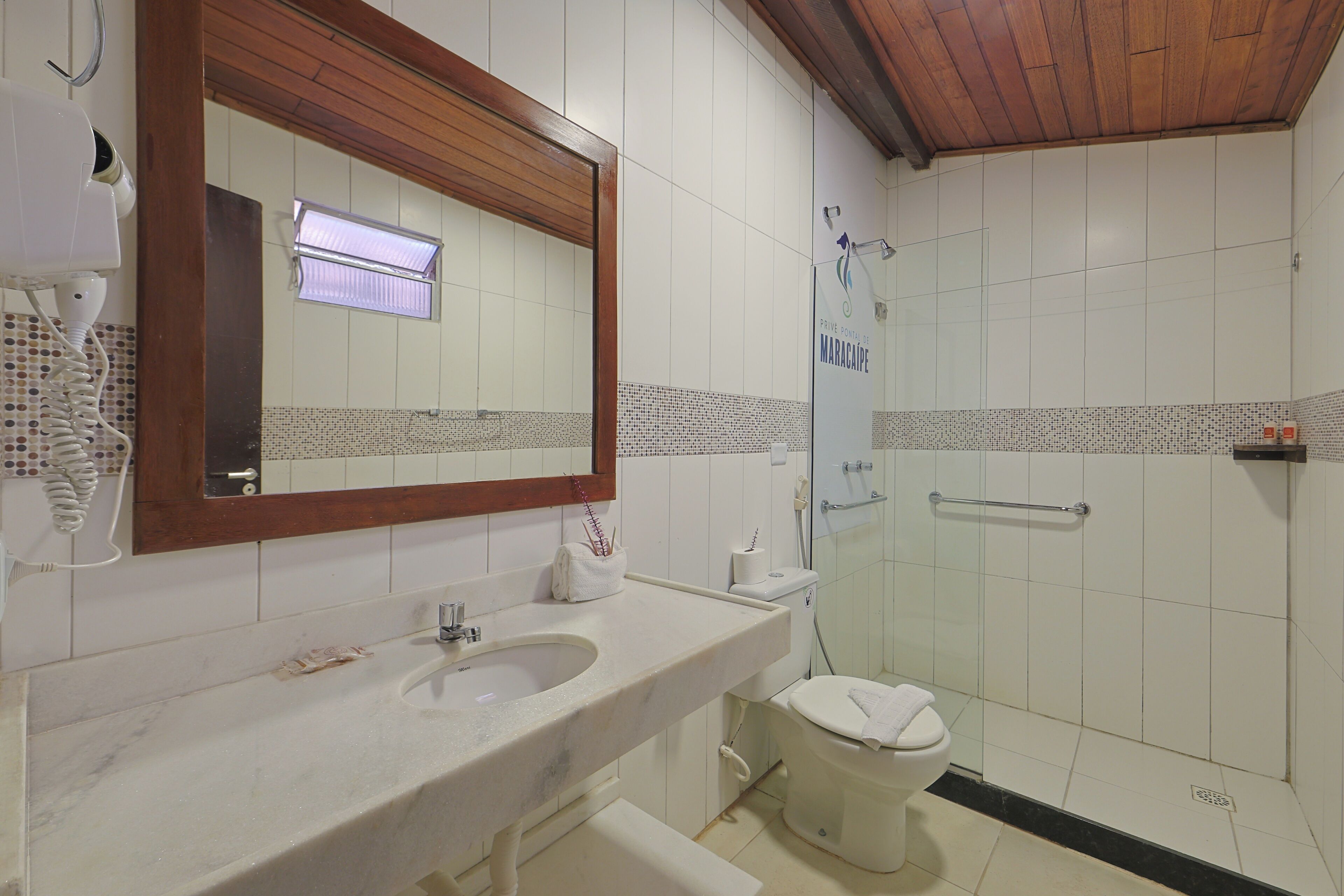 A bathroom with a marble sink, a toilet, a shower with a glass door, and a wooden ceiling.