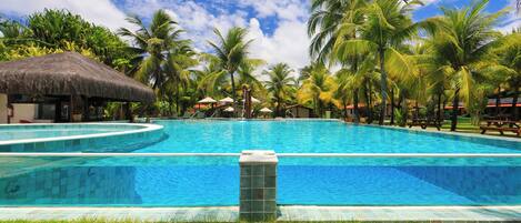 Una gran piscina rodeada de palmeras y una cabaña con techo de paja.