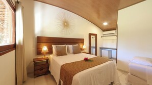 Une chambre à coucher avec une tête de lit en bois, une table de chevet avec une lampe, un grand lit recouvert d’un plaid marron et un miroir accroché au mur.